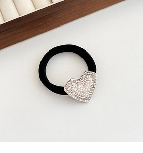 Detailed macro of heart-shaped charm with pearls and rhinestones on black elastic band