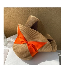 Detail of khaki straw sun hat featuring a vibrant orange bow and woven texture