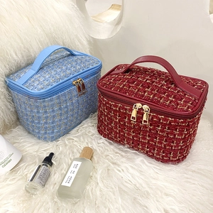Blue and red tweed makeup bags with gold zippers and handles on plush background