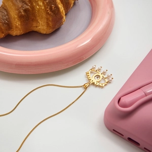 Detailed view of a gold evil eye necklace with white beads and zircon on a pink plate