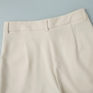 Detailed view of cream tailored trousers featuring twill texture and waist pleat design
