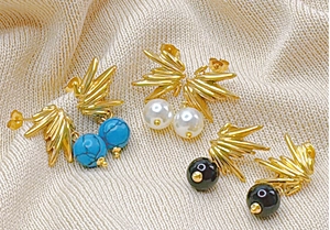 Détail de boucles d'oreilles plume dorées avec turquoise bleue et perles blanches