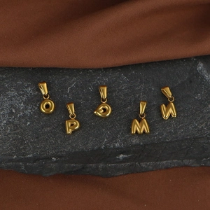 Macro shot of gold-plated stainless steel bubble letter pendants on dark textured stone