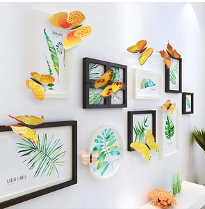 3D butterfly wall stickers in yellow and orange tones around framed plant art on a white wall