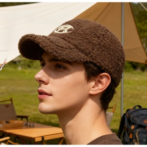 Close-up of brown teddy fleece baseball cap with bow embroidery in an outdoor setting