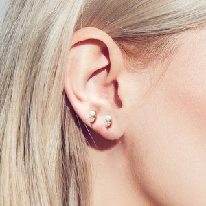 Close-up of small gold cartilage earrings with opal stones and zirconias on ear