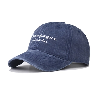 Close-up of deep blue washed cotton baseball cap with white 'Champagne please' embroidery