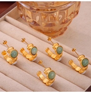 Detail view of five gold gourd earrings with green gemstones in a beige velvet box