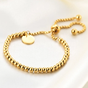 Close-up of 18K gold-plated beaded bracelet with adjustable round tag on silk fabric