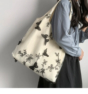 Detail of delicate black lace butterfly embroidery on a beige canvas tote bag with mesh layer