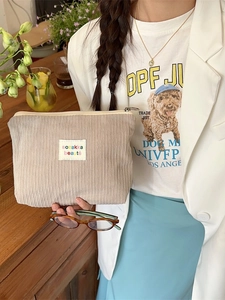 Vintage beige corduroy cosmetic bag with label held by model in casual indoor setting