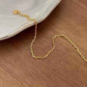 Detail of minimalist gold chain bracelet with heart charm on white porcelain plate