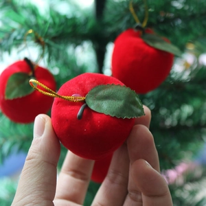 Close-up of red flocked Christmas apple ornament with green leaf on a green tree