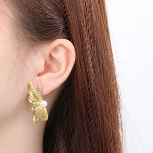Detailed close-up of a gold butterfly wing earring with a white pearl on a model