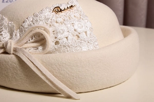 Detail of off-white wool beret with lace floral patch and bow with metal buckle