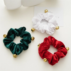 Three velvet hair scrunchies in green, white, and red with small gold bells for Christmas
