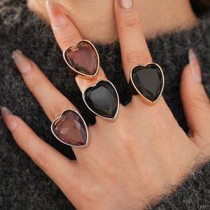 Detail of oversized heart-shaped zircon rings in gold and silver on a knit sweater