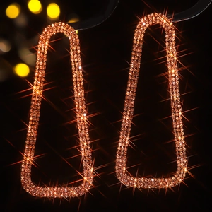 Macro shot of gold geometric trapezoid earrings with dense rhinestones and starburst effect