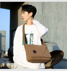 Brown canvas messenger bag shown on model against an industrial building background