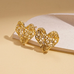 Detail of gold hollow heart earrings with lava texture and sparkling zircon accents