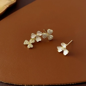 Detail of asymmetric gold flower earrings with white enamel and sparkling zircon accents
