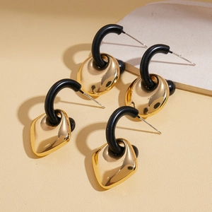 Elegant geometric gold and black dangle earrings with oval and diamond shapes on beige background