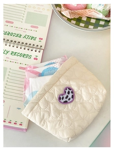 Dettaglio borsa trapuntata crema con ricamo cuore leopardo viola su tavolo bianco