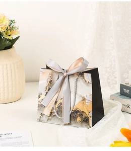 Detailed view of marble pattern gift bag with grey satin bow and elegant braided handle