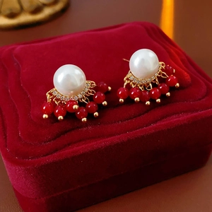 Detail of gold plated pearl earrings with red bead tassels on red velvet jewelry box