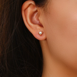 Close-up of minimalist pearl stud earring with golden four-prong setting on female ear