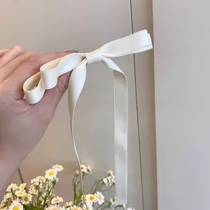 Detail of a creamy satin bow hair clip with long elegant ribbons in a soft finish