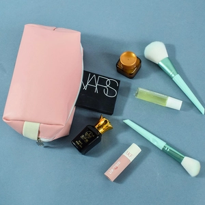 Detailed top view of a pink PU leather makeup bag with brushes and cosmetics on blue background