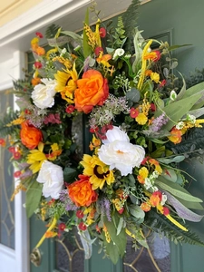 Close-up of vibrant faux eucalyptus wreath with roses and sunflowers on a green door