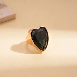 Détail macro d'une pierre verte géante en forme de cœur sur une large bague dorée