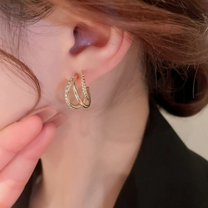 Close-up of gold double-layered C-shaped earrings with rhinestones and twisted texture