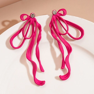Detailed view of pink ribbon bow earrings with rhinestone stud on ceramic tray