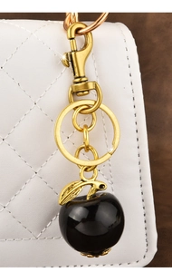 Detail of a golden apple keychain charm with a black glossy finish on a quilted white bag