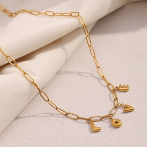 Detail of 18K gold-plated paperclip chain necklace with L O V E letter charms on fabric