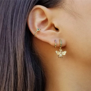 Detailed close-up of a gold bee pendant earring with green stones on a female model