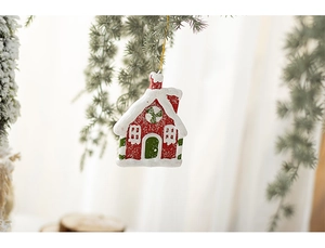 Detail of a festive resin house ornament hanging on a snowy pine branch in a warm setting