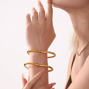 Polished 18k gold plated wave bangles with heart accent on female model wrist
