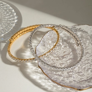 Close-up of gold and silver stainless steel bangles set with white zircon on glass