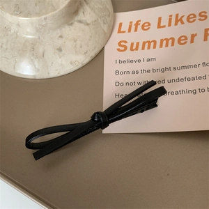 Close-up of a minimalist black leather bow hair clip on a marble and beige tray
