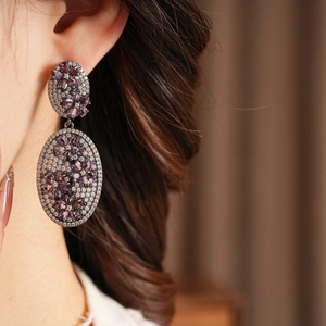 Detailed view of vintage oval earrings with purple floral gems and pave zircons on model