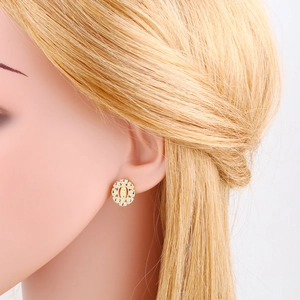 Detailed close-up of golden Virgin Mary stud earring with white zircon inlay on model ear