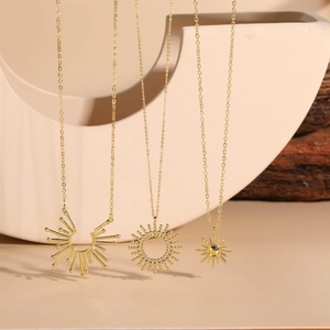 Detailed view of three 14K gold plated sunflower and starburst pendant necklaces on ceramics