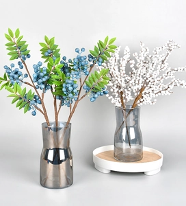 Detailed view of artificial blue and white berry stems in grey translucent glass vases
