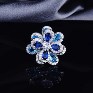 Blue and silver flower open ring with zircon crystals on a reflective surface