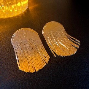 Macro shot of gold-tone metal fan fringe earrings on a black leather textured background
