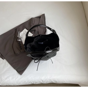 Minimalist black faux leather bucket bag displayed on white fabric with a stylish blazer